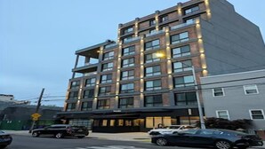 A multi-story hotel with a modern architectural design, featuring a prominent entrance and a parking area in front. - Dutch Hotel Long Island City New York , Belvilla District 6 Formerly Sonder (New York)