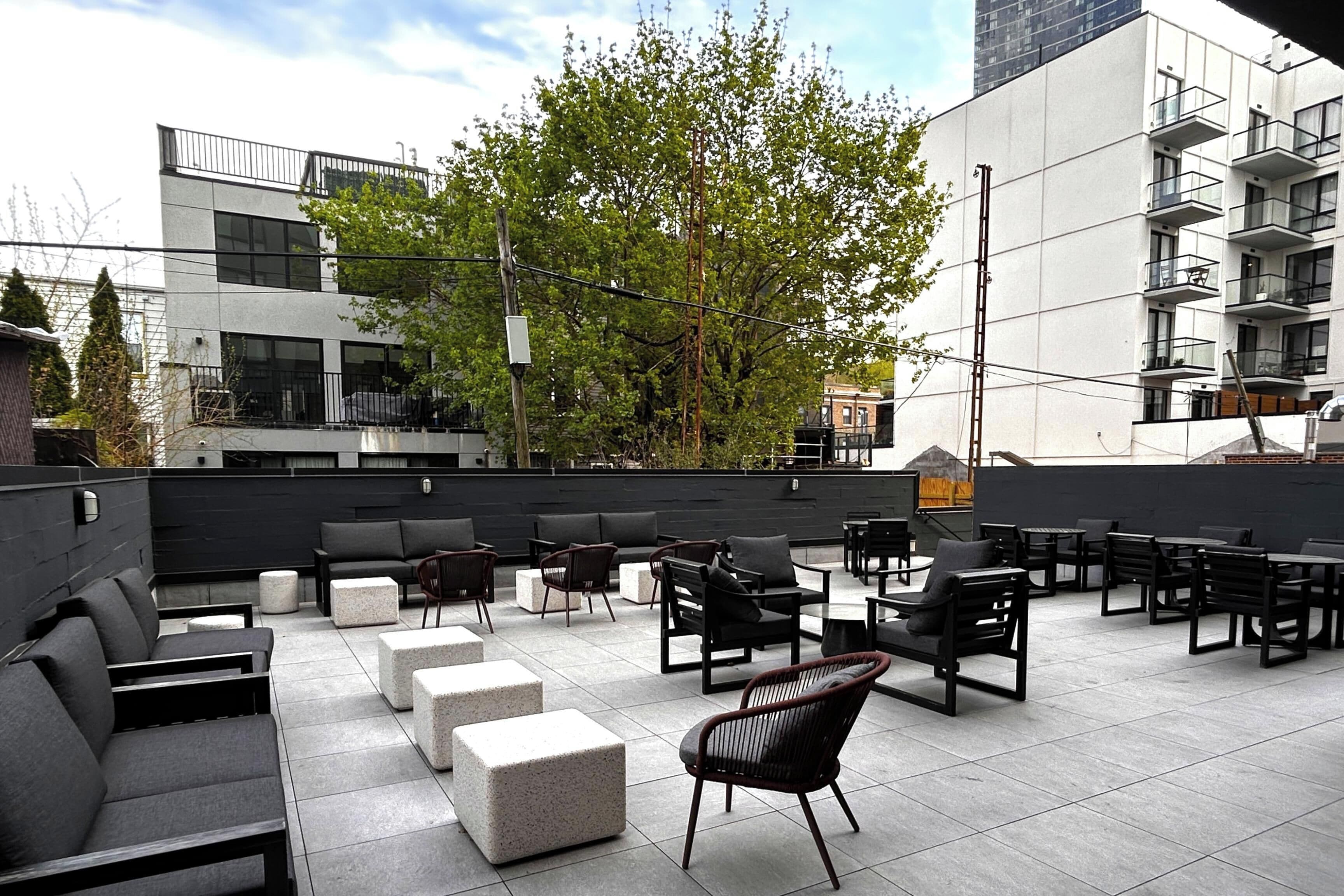 An outdoor seating area with modern furniture, a tree, and a building in the background.