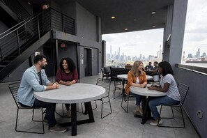 Una terraza en la azotea con mesas y sillas redondas, una escalera y vistas del horizonte urbano.