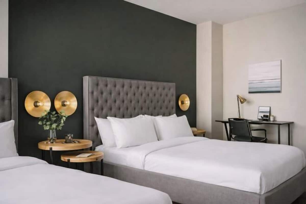 A hotel room with a tufted headboard, two round tables, a desk, and a bed with white bedding.