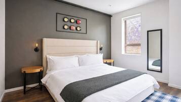 A modern bedroom with a large bed, a headboard, bedside tables, a wall clock, a window, and a mirror.