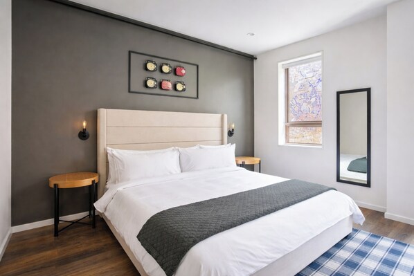 Un dormitorio moderno con una cama grande, cabecera, mesitas de noche, un reloj de pared, una ventana y un espejo.