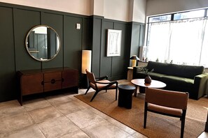Una habitación con una pared verde oscuro, un espejo redondo, un sofá, dos sillones, una mesita y una ventana con cortinas.