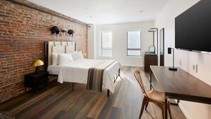 A modern hotel room with a brick wall, a large bed, a wooden floor, a desk, and a flat-screen TV. - Dutch Hotel Long Island City New York , Belvilla District 6 Formerly Sonder (New York)