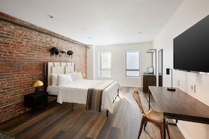 A modern hotel room with a brick wall, a large bed, a wooden floor, a desk, and a flat-screen TV. - Dutch Hotel Long Island City New York , Belvilla District 6 Formerly Sonder (New York)