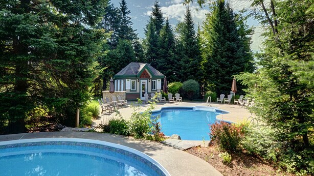 Un área de piscina con dos piscinas, un edificio pequeño y árboles circundantes.