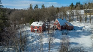 Une cabane rouge, dont le toit est recouvert de neige, entourée d’une forêt et sous un ciel dégagé.