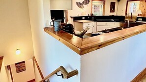 Une cuisine avec un îlot central en bois, des murs blancs et un escalier menant à un autre niveau.