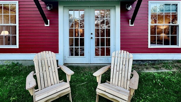 Une maison rouge avec une porte bleue et deux chaises en bois devant.