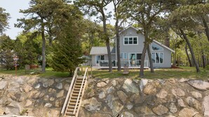 A house with a stone retaining wall and a wooden staircase leading up to it. - Make memories at this unique family friendly beach-front home in Mashpee  (Mashpee)