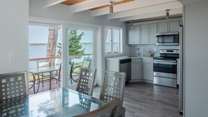 A modern kitchen with a glass dining table, wooden flooring, and a view of the outdoors. - Make memories at this unique family friendly beach-front home in Mashpee  (Mashpee)