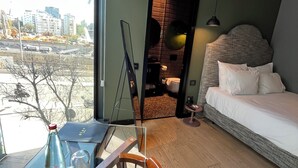 Een moderne kamer met een glazen tafel, een houten stoel, een bed en uitzicht op de stad.