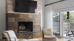 A modern living room with a stone fireplace, leather armchairs, a coffee table, and a flat-screen TV mounted on the wall. - Outpost: Timber Ridge 9 - Spacious Deck, Hot Tub & Pool Access! (Teton Village)