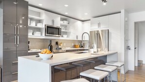 A modern kitchen with a central island, bar stools, stainless steel appliances, and white cabinetry. - Outpost: Timber Ridge 9 - Spacious Deck, Hot Tub & Pool Access! (Teton Village)