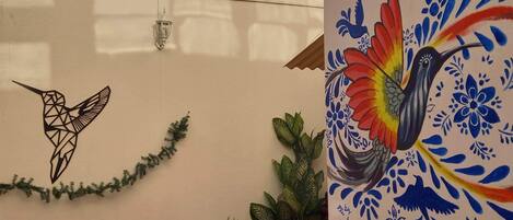 A wall with a geometric hummingbird mural and a colorful bird painting.