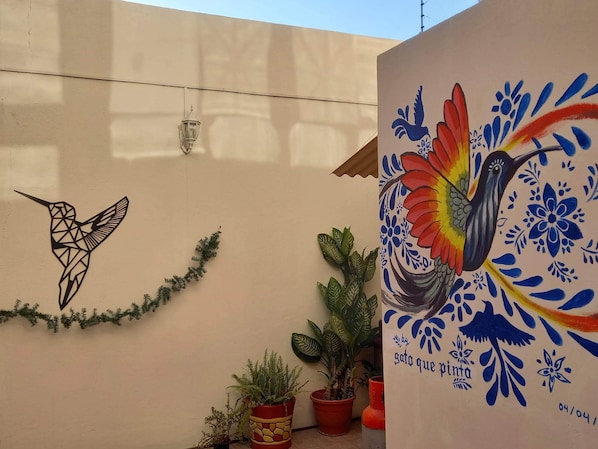 A wall with a geometric hummingbird mural and a colorful bird painting.