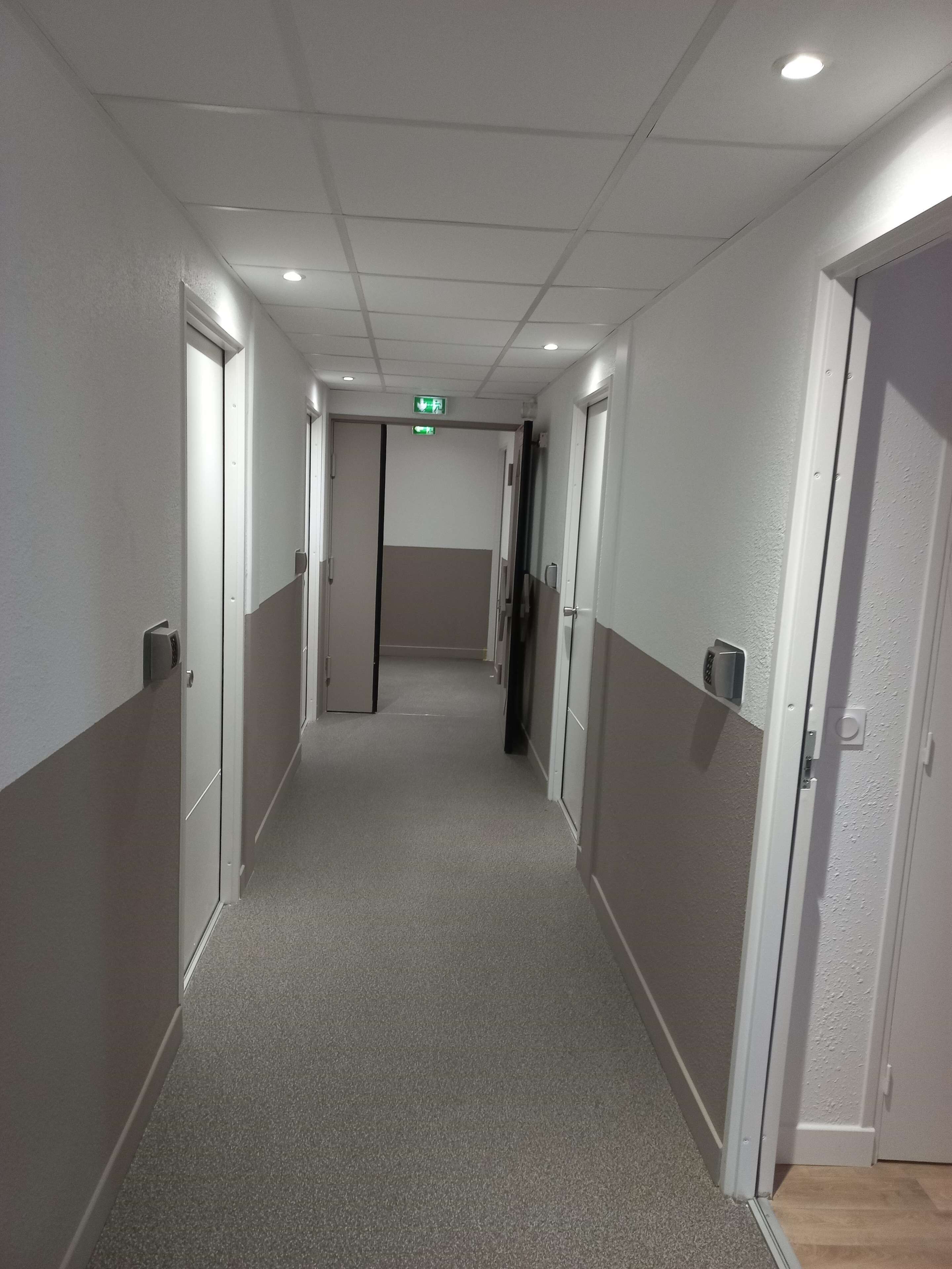A corridor with doors on both sides, a carpeted floor, and a ceiling with recessed lighting.