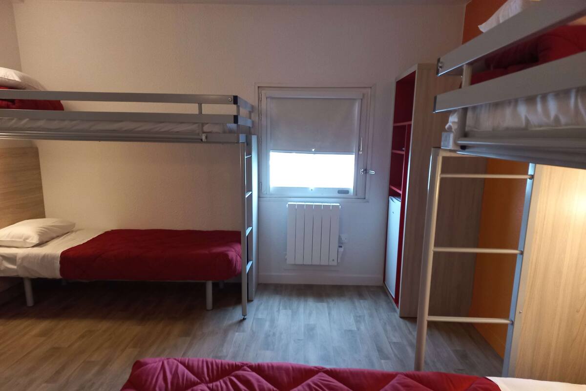 Ein Schlafsaalzimmer mit Etagenbetten, einem Fenster, einem Heizkörper und einem Kleiderschrank.