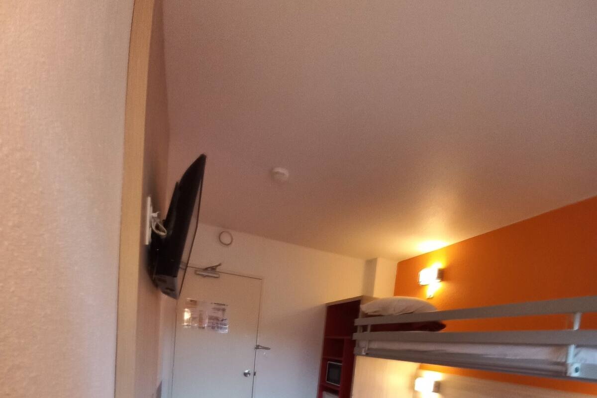 Ein Zimmer mit zwei Betten, einem an der Wand befestigten Fernseher, einer Tür und einer Wandleuchte.