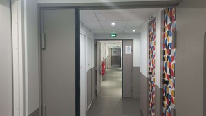 Een gang met een vluchtwegbord, een brandblusser en een behang met patroon.