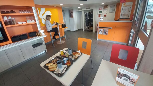 Een café met oranje en witte decoratie, een persoon zit aan een tafel en er staan verschillende gerechten op dienbladen.