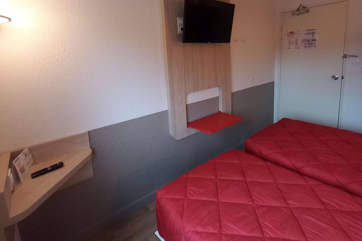 Ein Zimmer mit einem Bett, einem Wandfernseher, einem Holzregal und einer Tür mit einem Poster.