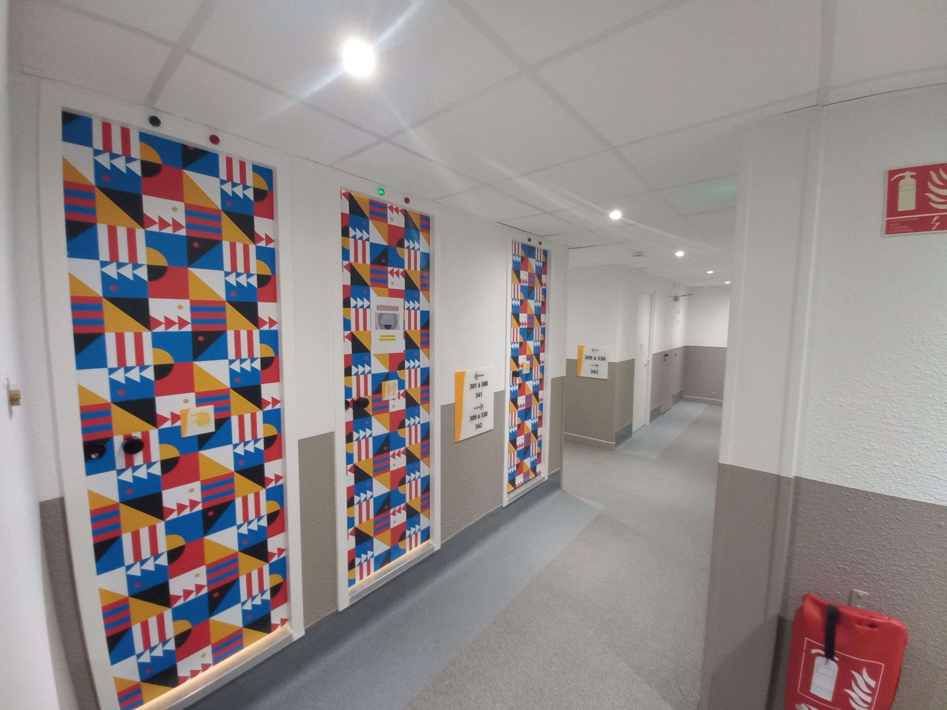 Een gang met kleurrijke geometrische wanddecoraties, bewegwijzering en een brandblusser aan de rechterkant.