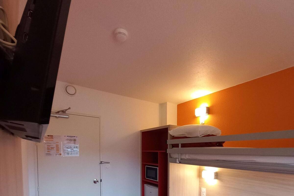 Ein Schlafzimmer mit Etagenbetten, einem Fernseher, einer Tür und einem kleinen Kühlschrank.