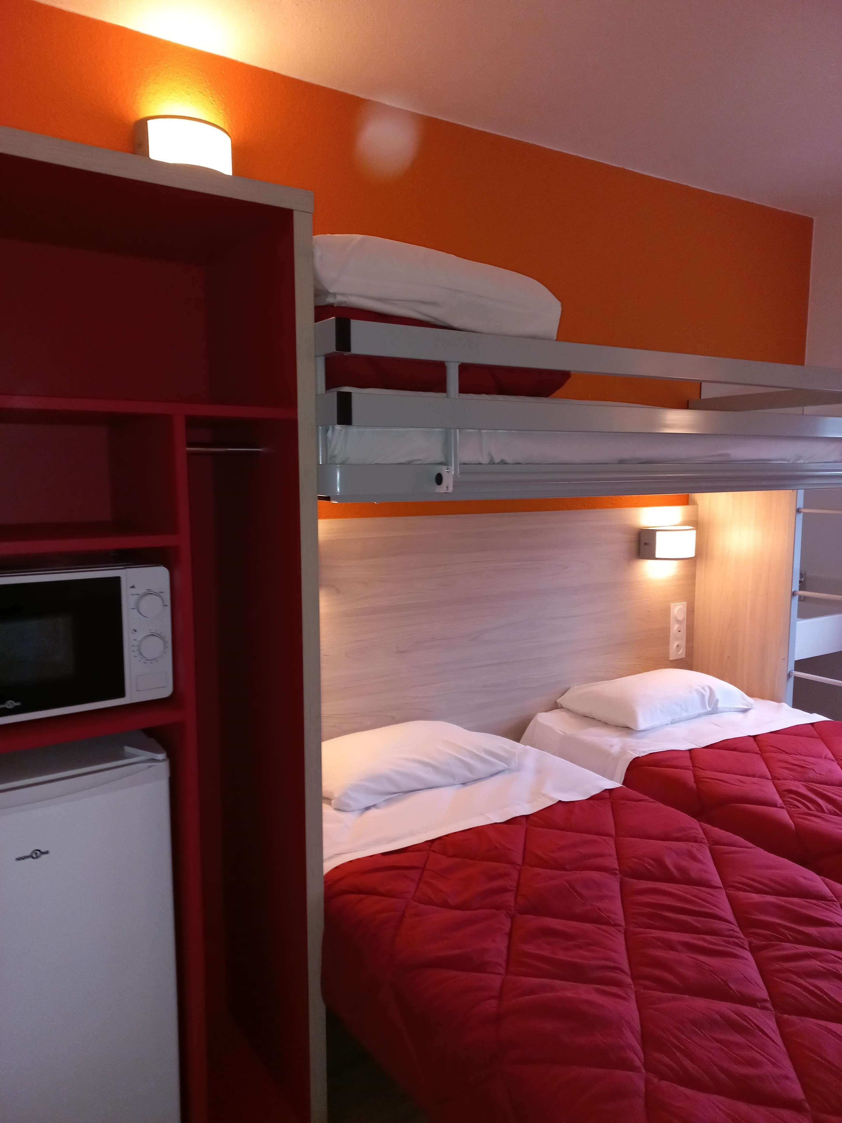 A bunk bed with a red blanket, a microwave, and a small refrigerator in a room with orange walls.