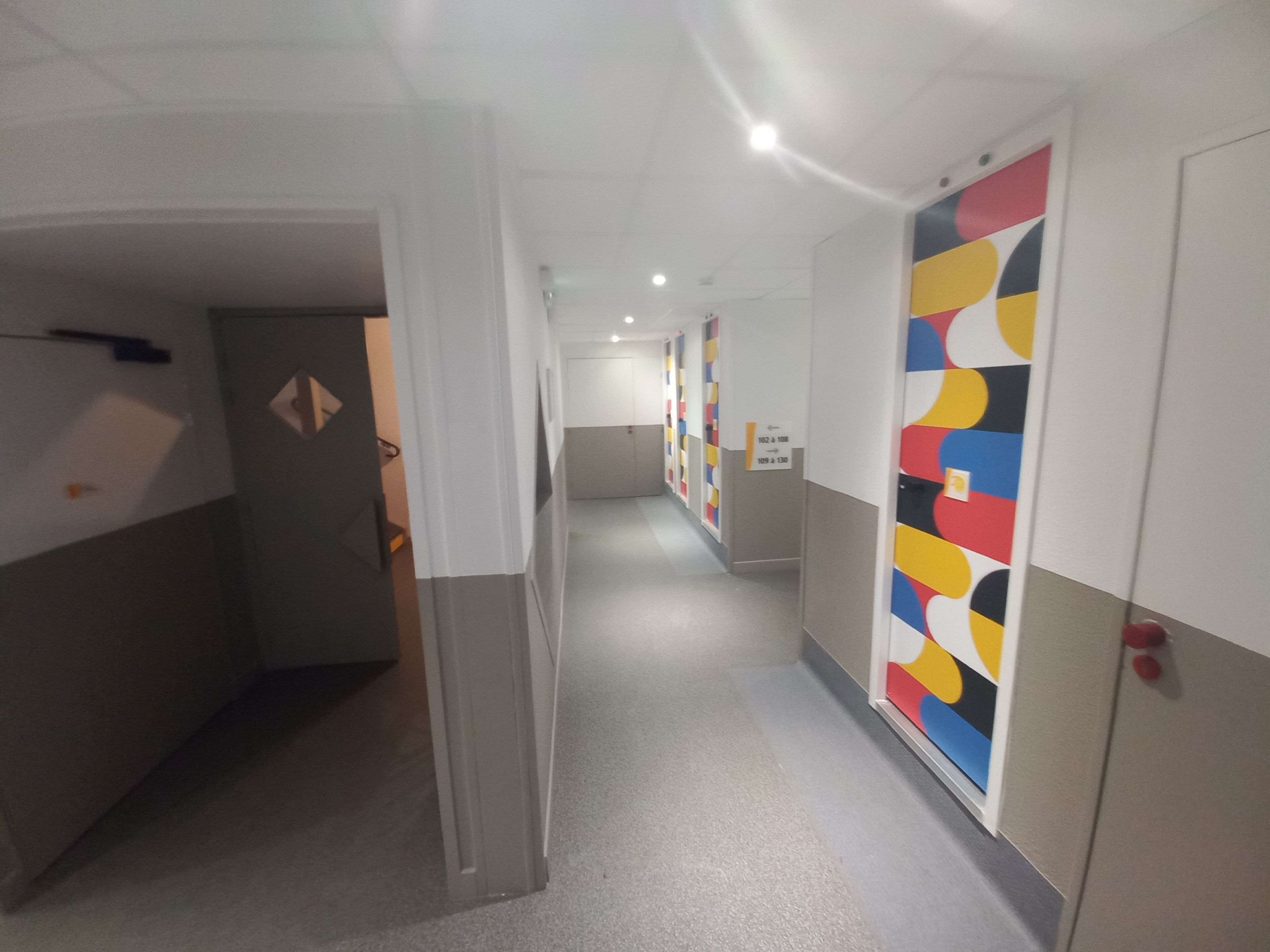 A corridor with lockers, a door with a sign, and a wall with a geometric pattern.