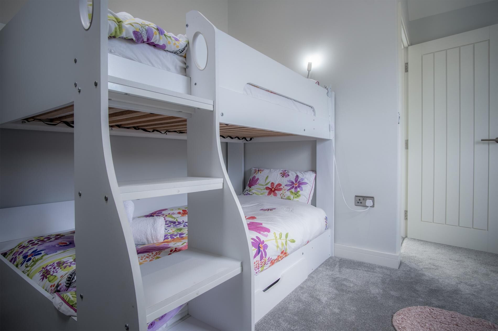 A bunk bed room with floral bedding, a grey carpet, and a white door.