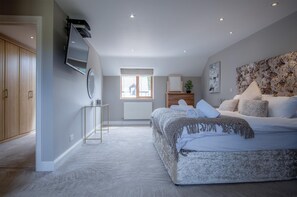 A bedroom with a large bed, a TV mounted on the wall, a dresser, and a window with blinds. - Knights Rest - 4 Bed Holiday Home - Princes Gate (Narberth)