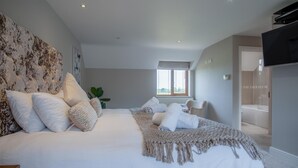 Ein Schlafzimmer mit einem großen Bett, einem Nachttisch, einer Pflanze und Blick ins Badezimmer.