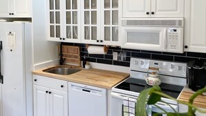 Una cocina con armarios blancos, microondas, hervidor y lavavajillas.