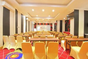 Un salón de conferencias con filas de mesas y sillas, un escenario con una pantalla de presentación y un suelo cubierto de alfombra roja.