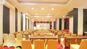 A conference room with rows of tables and chairs, a stage with a podium, and a red carpeted floor.