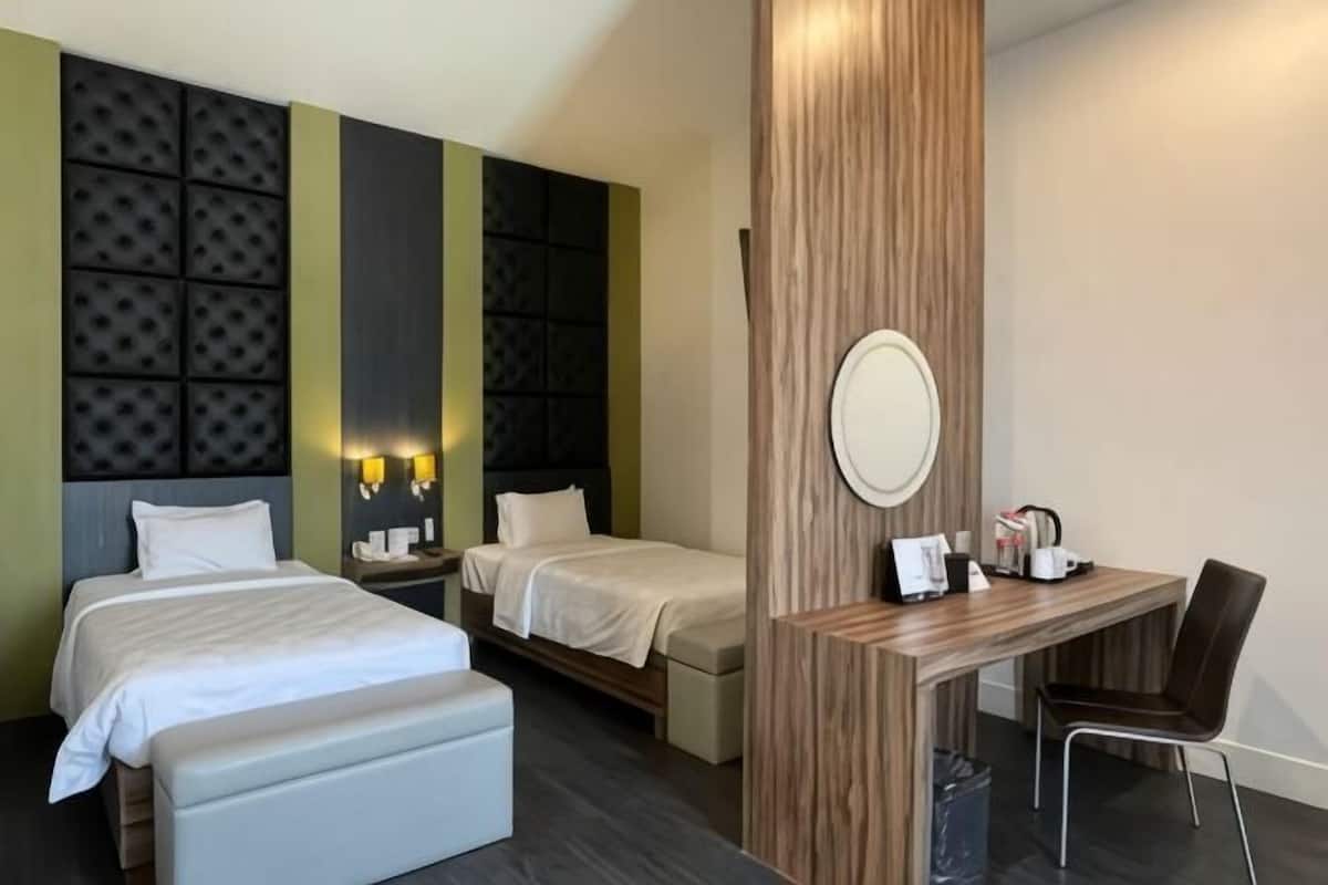 A hotel room with two beds, a desk, a chair, a mirror, and a small table with a kettle.