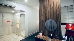 A hotel lobby with a reception desk, a wooden accent wall, a round mirror, and a red wall with a light fixture.
