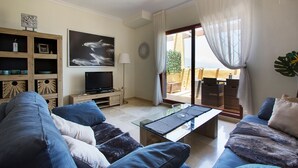Una sala de estar con un sofá, una mesa de centro, un televisor y un ventanal con cortinas.
