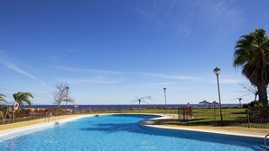 Piscina con vista al océano, rodeada de palmeras y una valla.