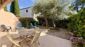 Un patio con un tavolo e sedie di legno, circondato da un giardino con alberi e fiori.