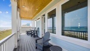 A covered deck with wooden flooring, a railing, and a view of the beach and ocean.