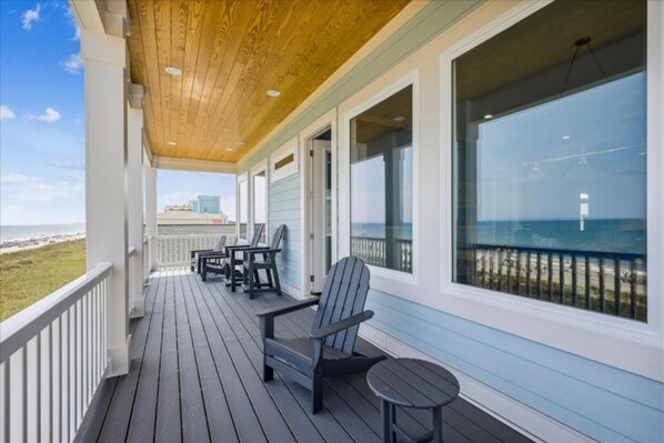 Una terraza techada con piso de madera, barandilla y vista a la playa y al océano.