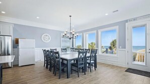 A modern kitchen with a central island, a dining area with a large table and chairs, and a view of the ocean through large windows.