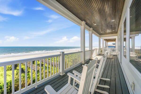 A covered deck with white railings overlooking a beach.