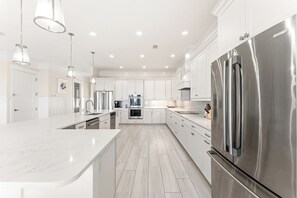 A modern kitchen with white cabinetry, stainless steel appliances, and a marble countertop.