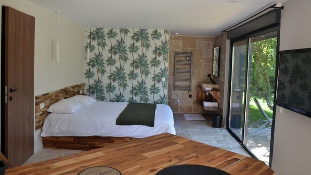Una camera da letto con un letto, un tavolo di legno, un bagno con doccia e un'ampia finestra vista verde.