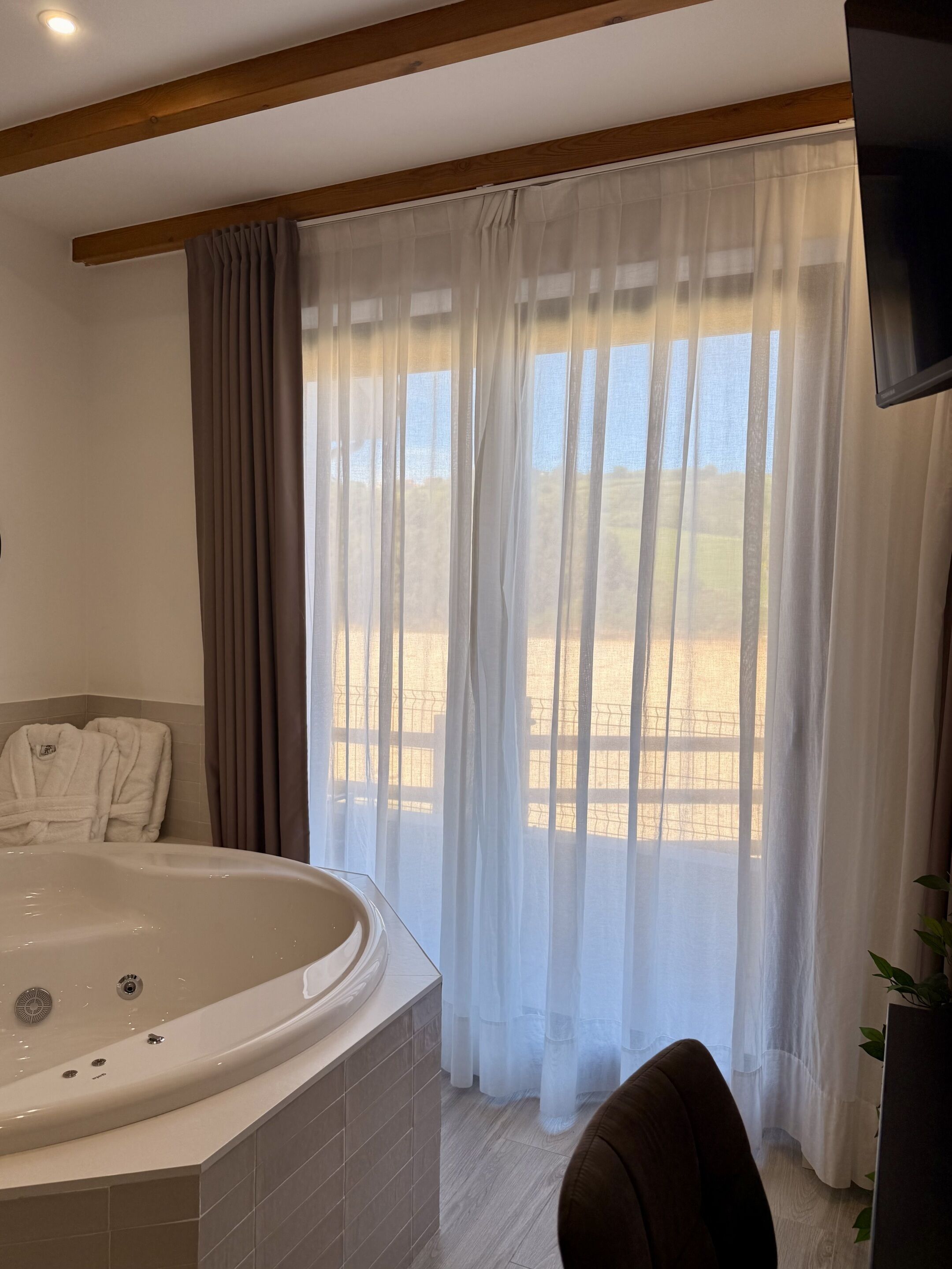 Un baño moderno con una bañera independiente, zona de ducha y un amplio ventanal con cortinas translúcidas.