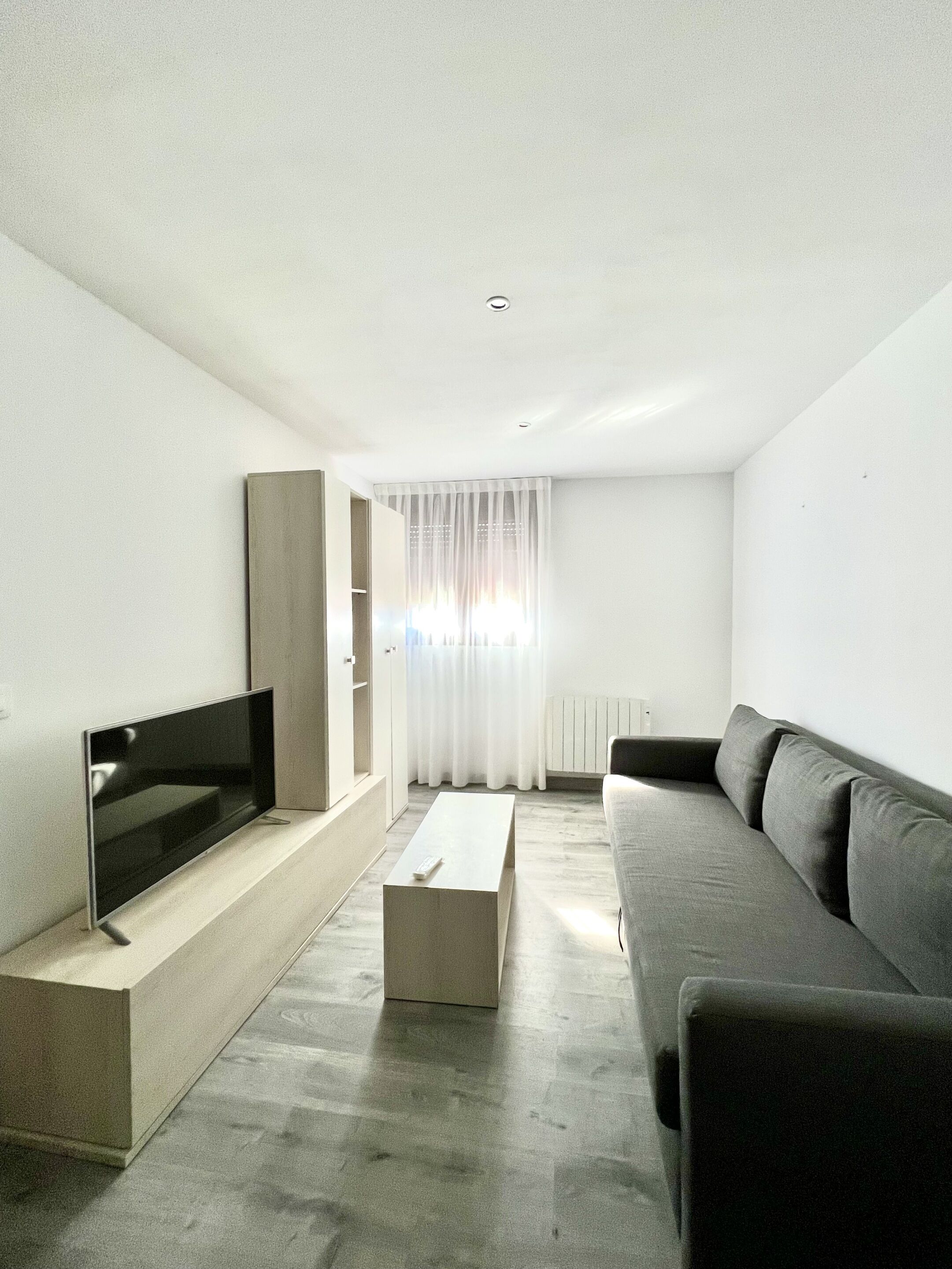 A modern living room with a flat-screen TV, a grey sofa, and a coffee table.