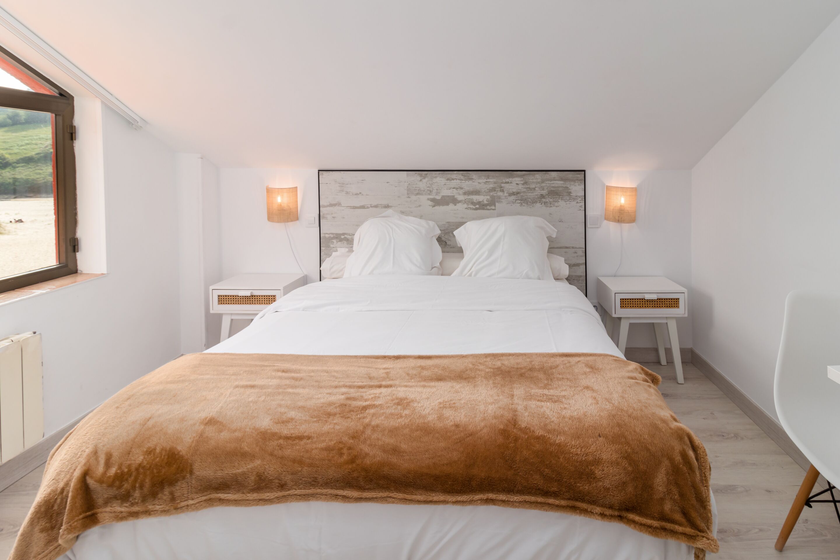 A bedroom with a large bed, two bedside tables, a nightstand, a window, and a view of the outdoors.